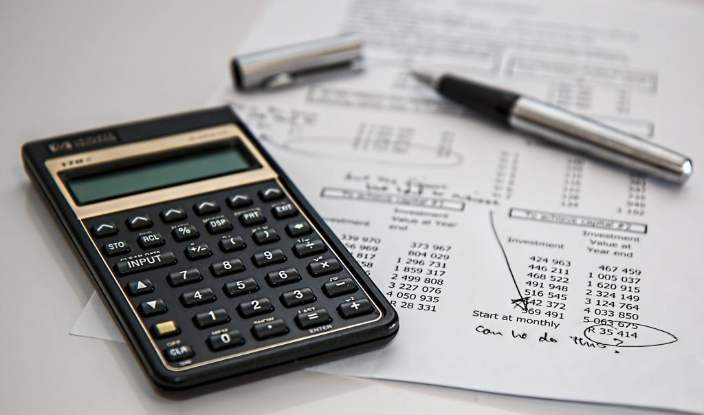 Calculator sitting on paper with financial calculations and a silver pen with the lid off