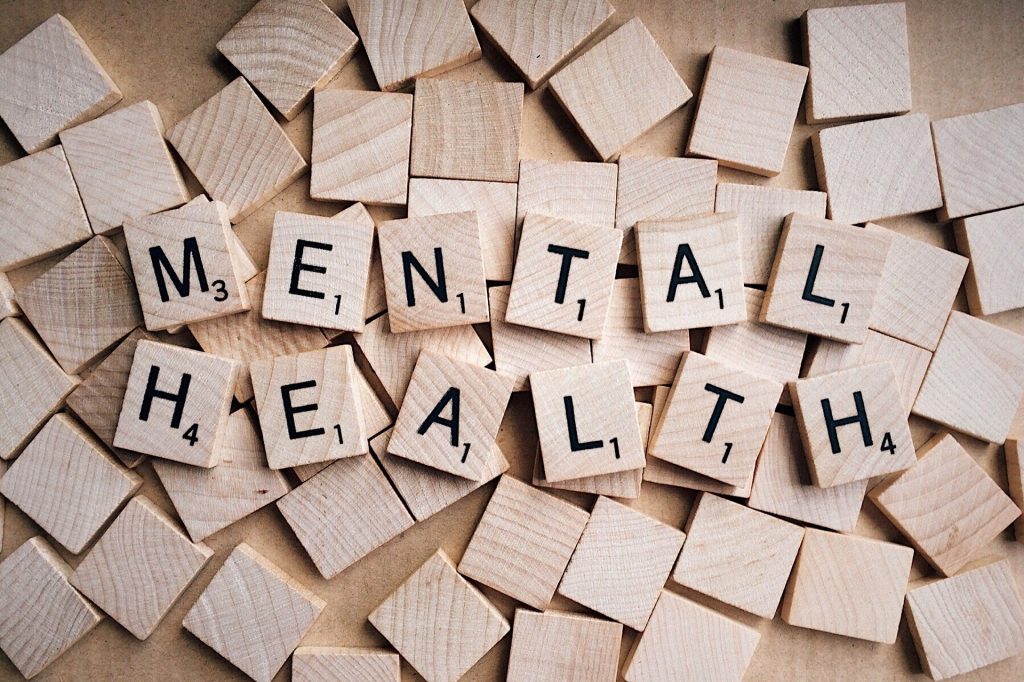 Pile of wooden scrabble tiles with some arranged to spell out mental health