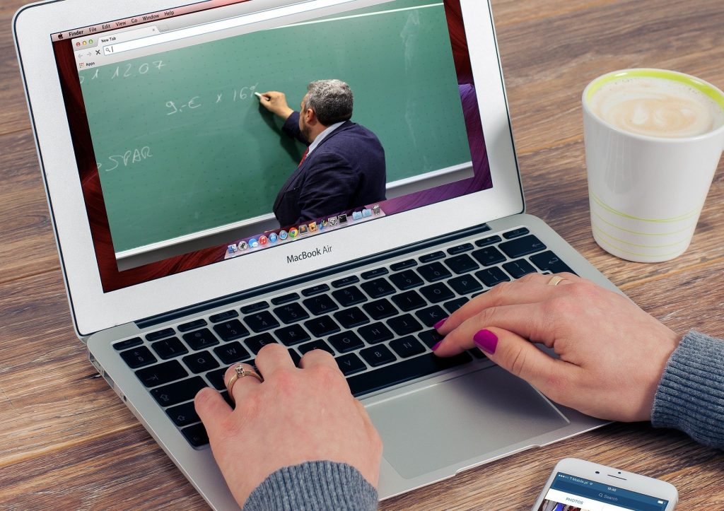 Open Macbook laptop on desk with two hands on keyboard and image of a man writing on a chalkboard