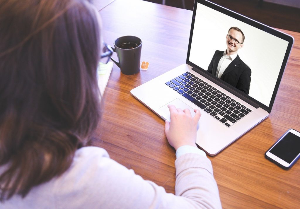 Woman sitting at desk with open laptop and image of smiling man on laptop