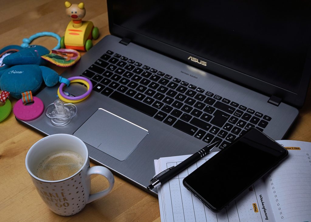 Open laptop on table with pen and notepad on one side and baby toys on the other